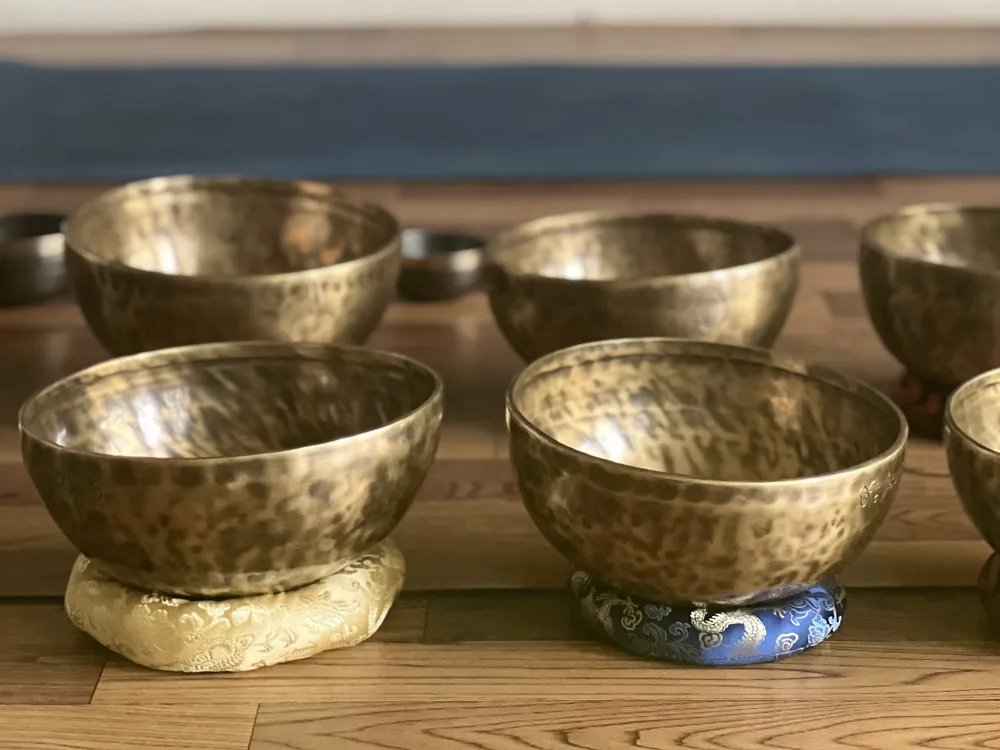 Hand-hammered brass singing bowls resting on cushions on a wooden floor