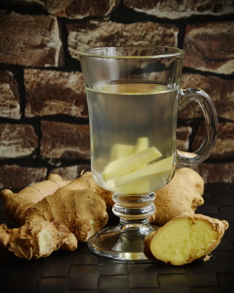 A glass of warm ginger tea beside fresh, sliced ginger root