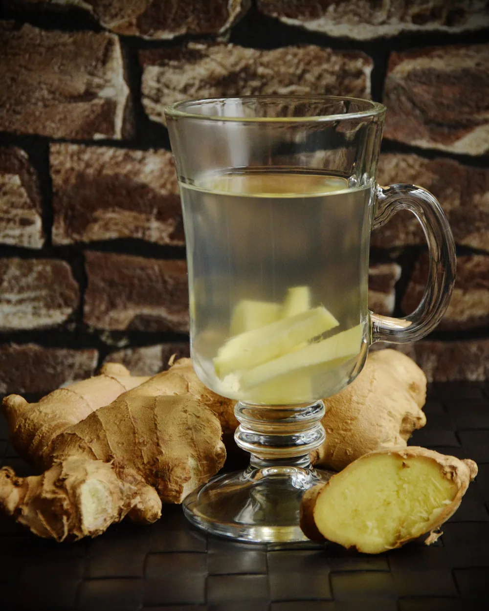 A glass of warm ginger tea beside fresh, sliced ginger root